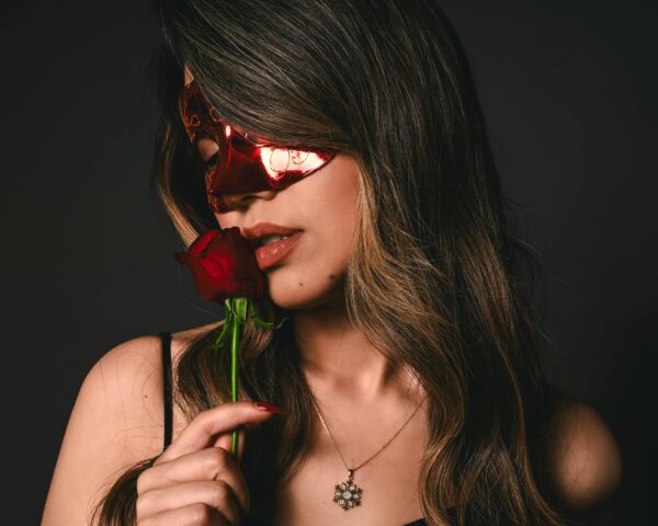 A woman wearing red mask touching red rose to her lips  